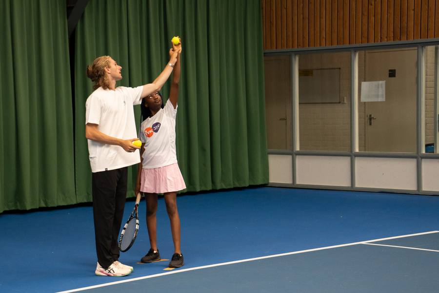 Coach begeleidt een jonge speelster bij de opslag tijdens indoor tennisles in Amstelveen — 359.tennis